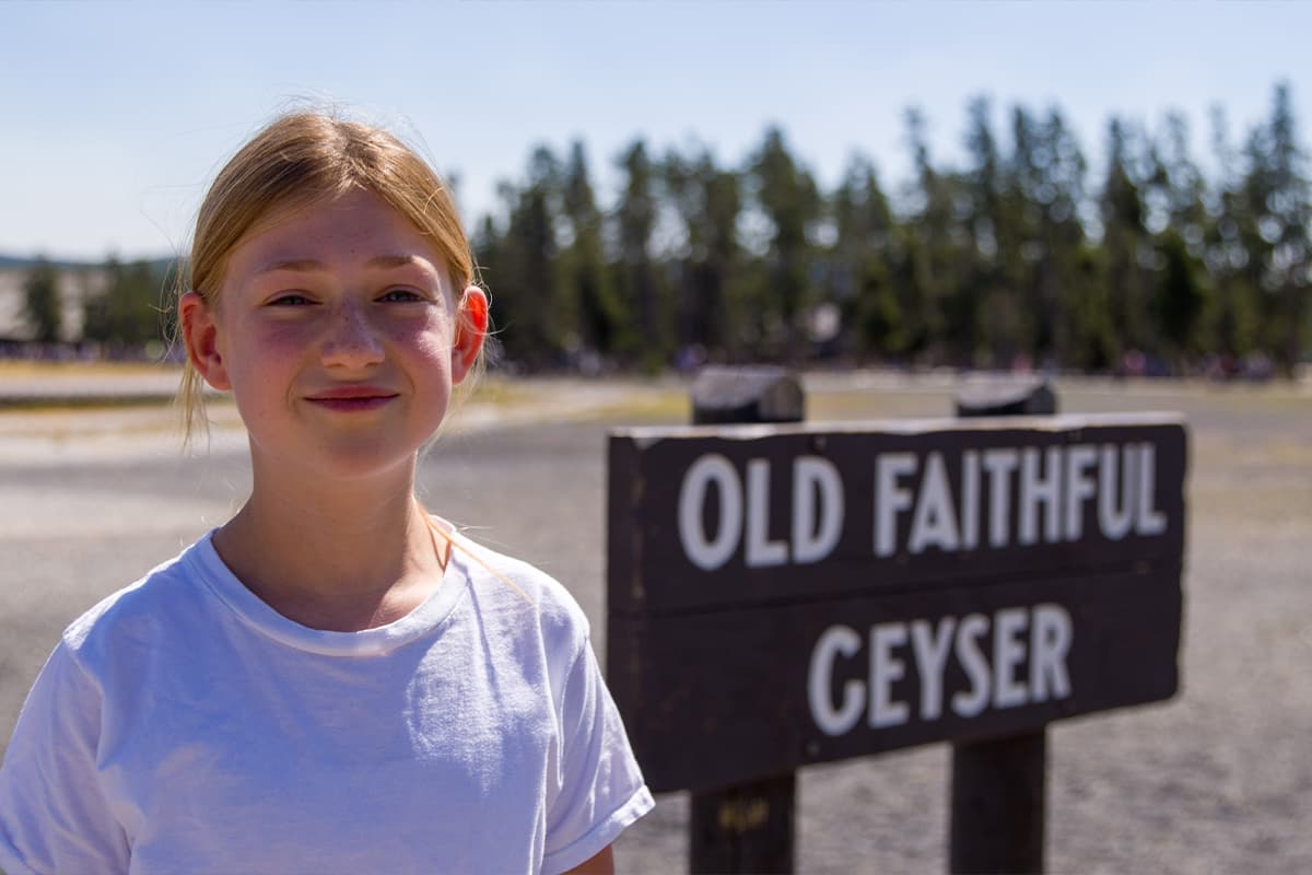 Adolescent girl standing in front of sign at Old Faithful Geyser