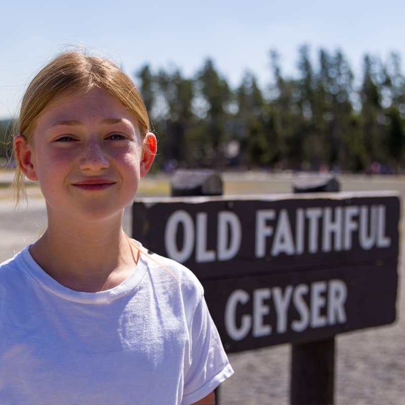 Adolescent girl standing in front of sign at Old Faithful Geyser